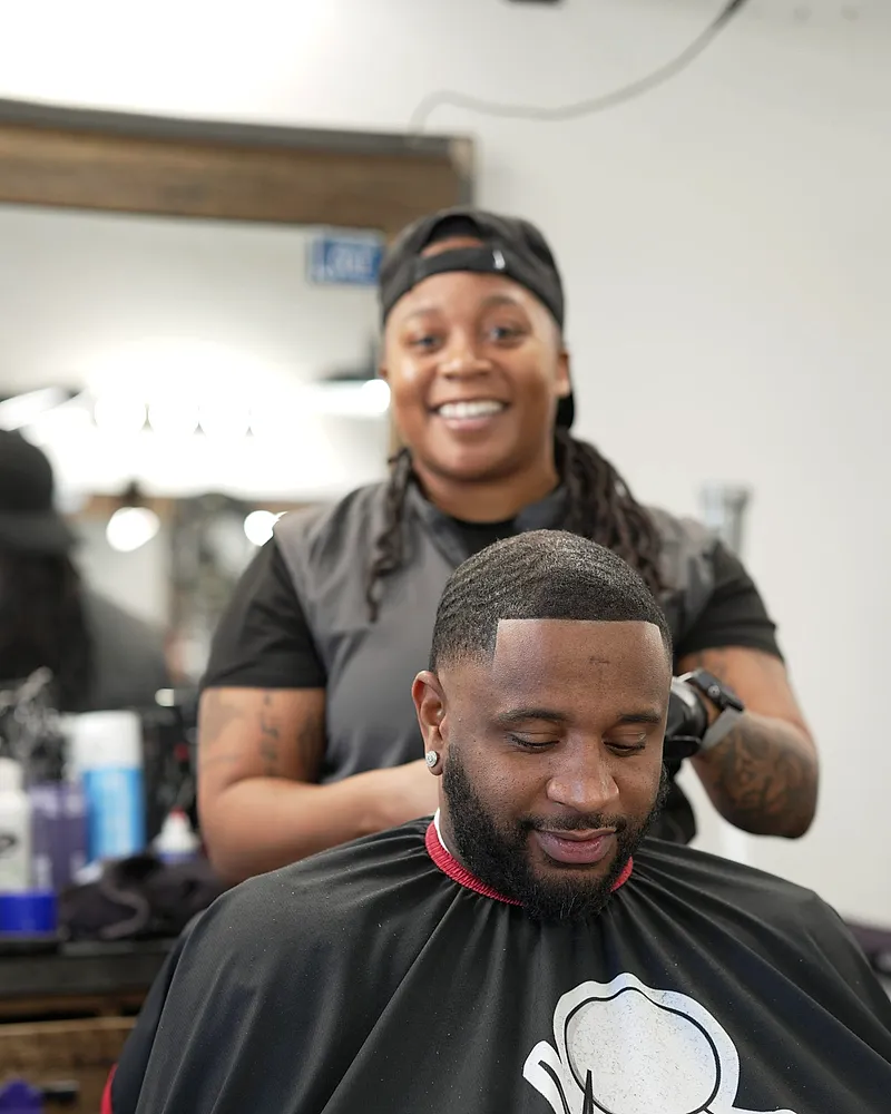A barber smiling while cutting a client's hair